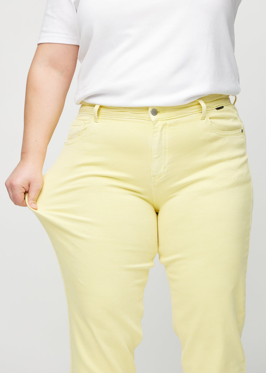 Regular jeans for women in light yellow, color Lemonades. A plus-size model stretches the fabric at the thigh to show its stretch.