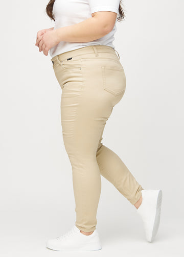 Beige skinny jeans seen from the side on a plus-size model.