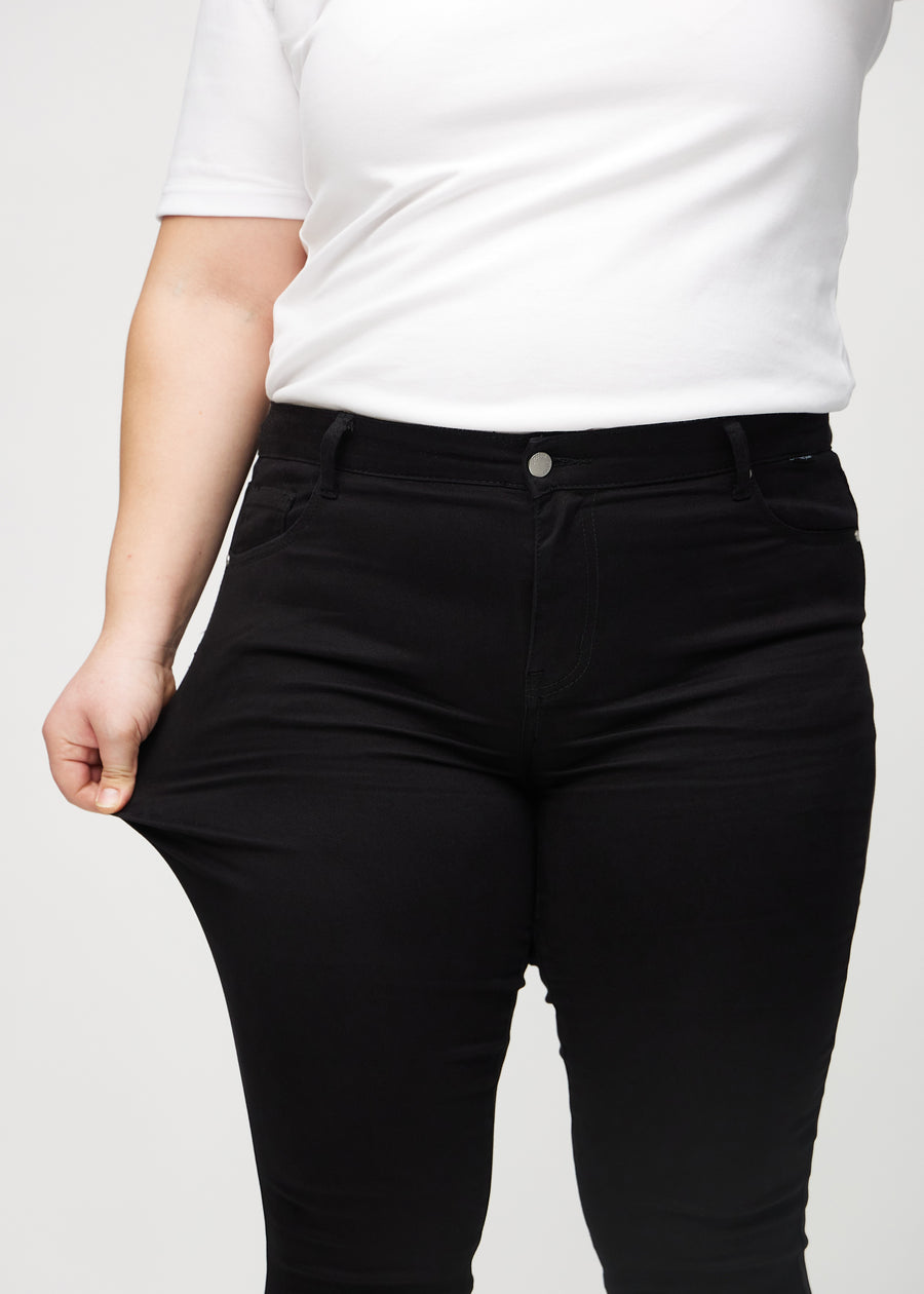 The plus-size model stretches the jeans at the thigh to show the stretch.