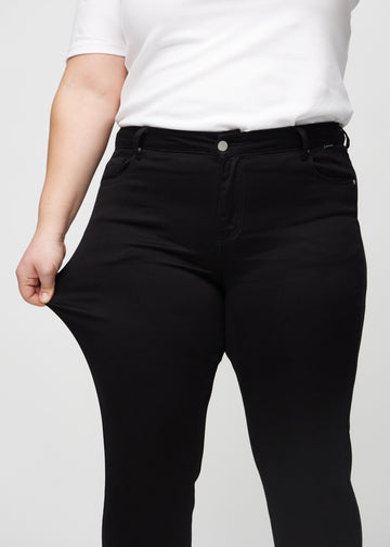 The plus-size model stretches the jeans at the thigh to show the stretch.