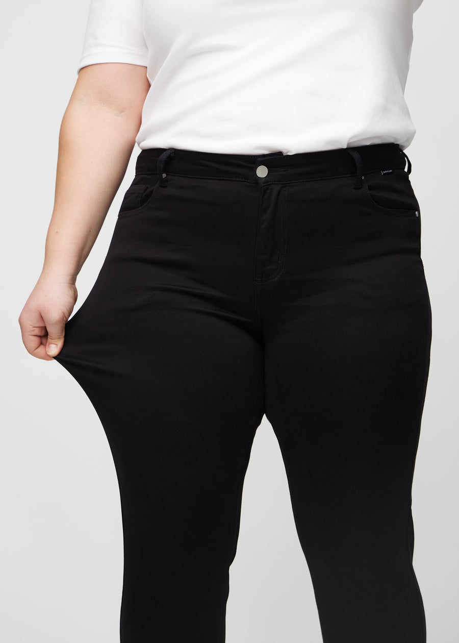 The plus-size model stretches the jeans at the thigh to show the stretch.