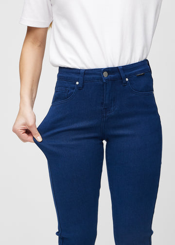 Slim jeans for women in dark blue, color Royals. A model stretches the jeans at the thigh to show the fabric&