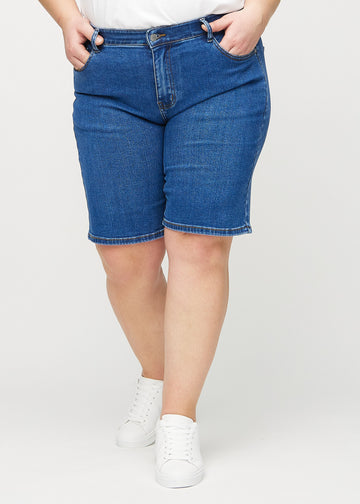 Dark denim regular middle shorts, model name Oceans, which go straight down the leg and end just above the knee on a plus-size model, seen from the front.