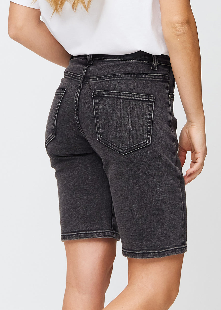 Woman in knee-length dark grey denim shorts seen from the back, so the denim details can be seen