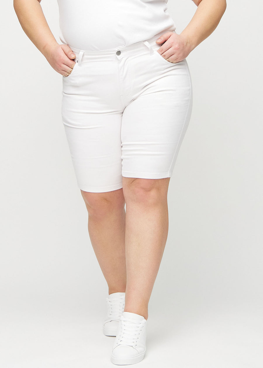 White skinny middle shorts, model name Marguerites, which fit tightly around the thigh and end just above the knee on a plus-size model, seen from the front.