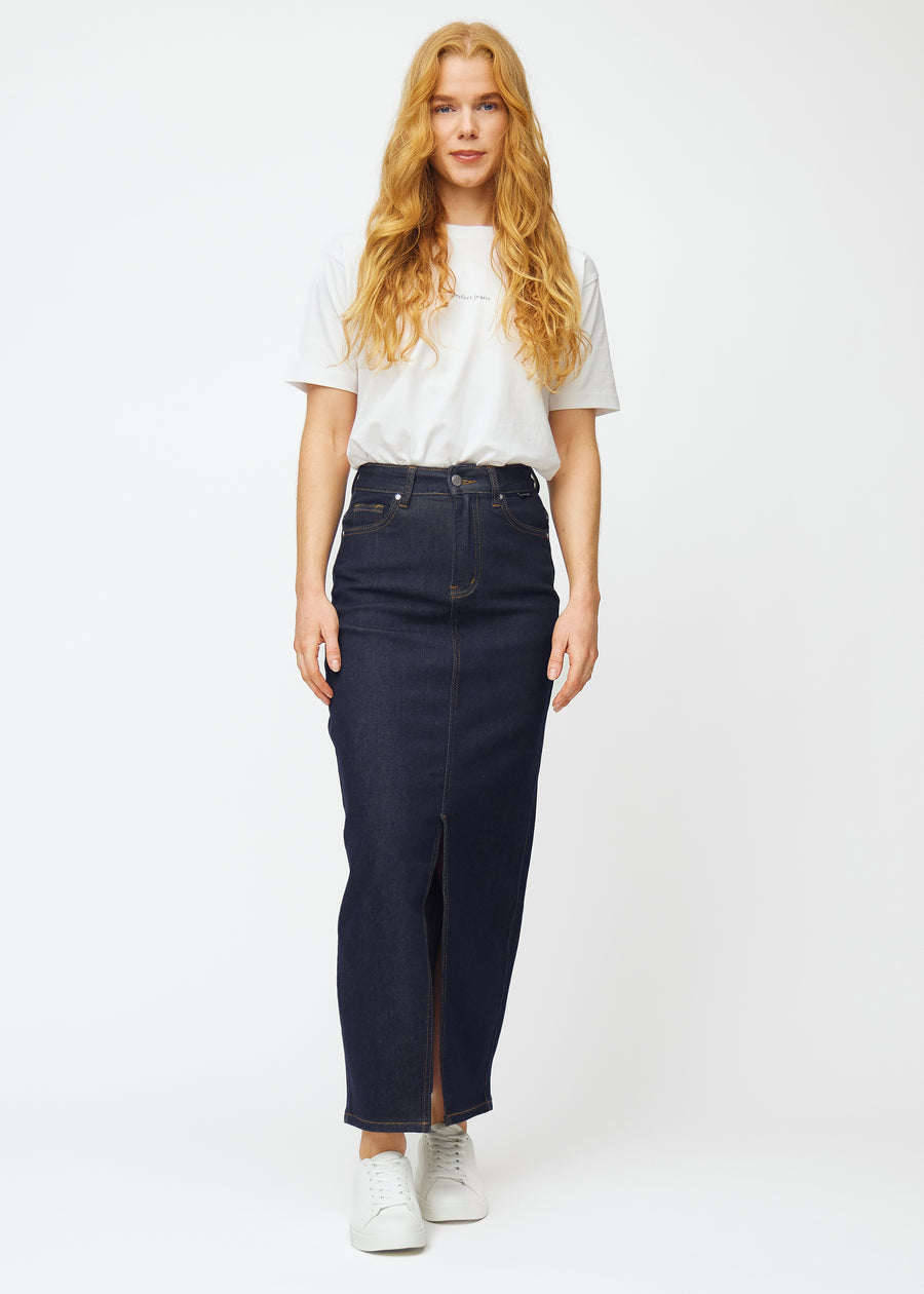 Full image of a model wearing a long deep dark blue denim skirt for women in the colour Midnights with a front slit.