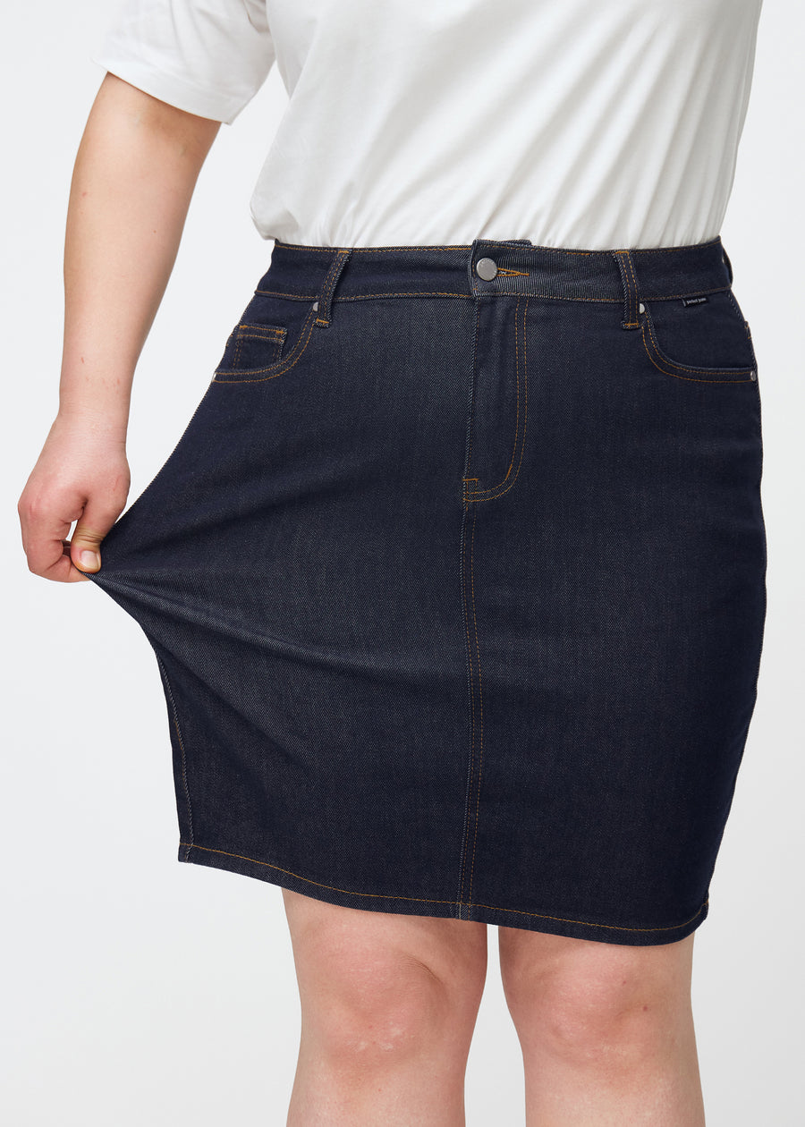 Plus-size model stretches deep dark blue denim skirt for women in the colour Midnights at the thigh to show stretch.