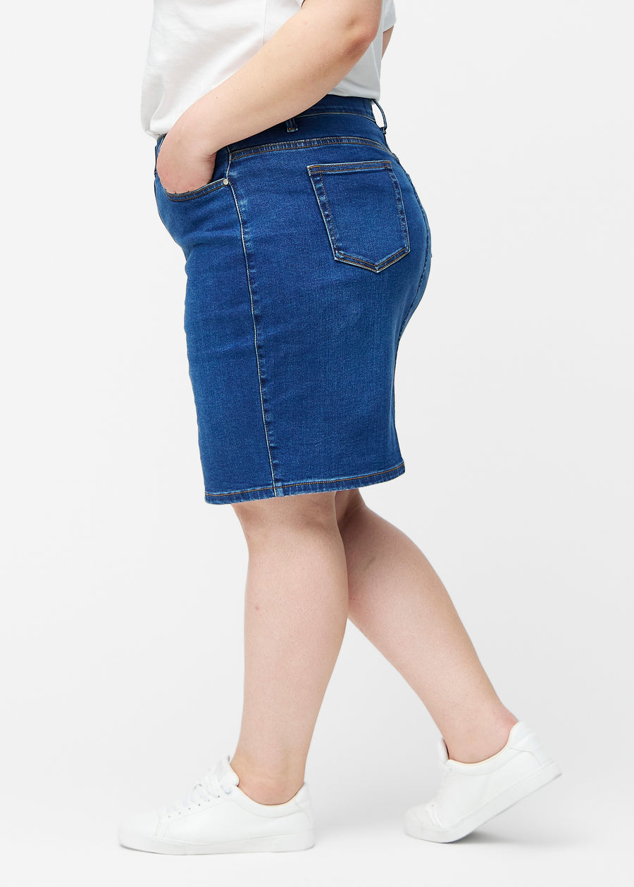 Mørkeblå, tætsiddende og knælang denimnederdel set fra siden på plus-size model.