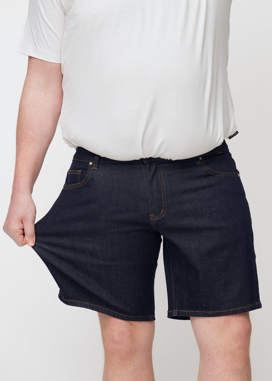 plus-size model stretches deep dark blue denim shorts for men in the colour midnights at the thigh to show stretch.