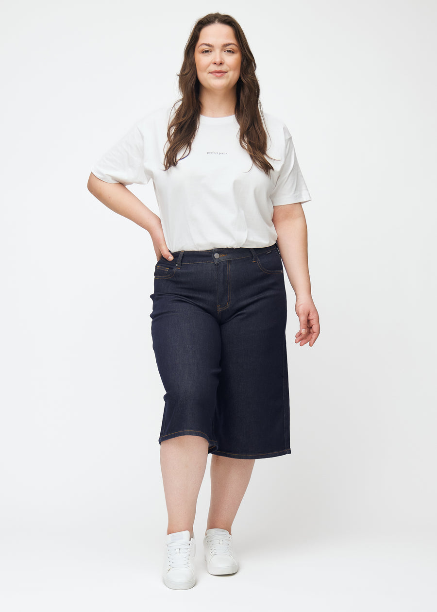 Plus-size model viser dyb mørkeblå denim capris til kvinder i farven Midnights med loose pasform i bevægelse.