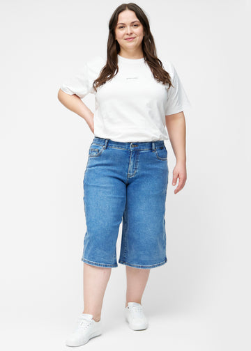 Plus-size model viser løse, klassisk blå denim capris i farven Rivers i bevægelse og demonstrerer pasform og materiale.