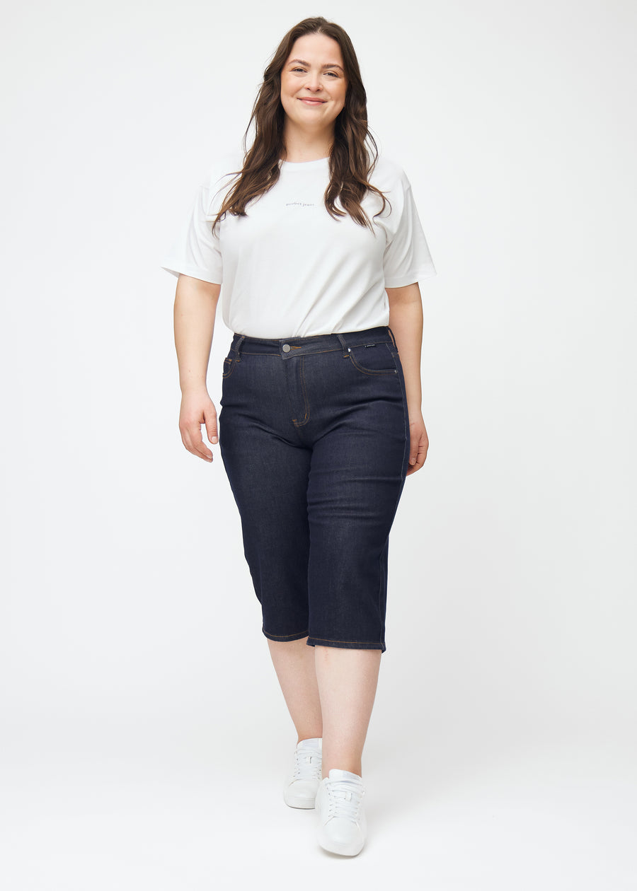 Plus-size model viser dyb mørkeblå denim capris til kvinder i farven Midnights med regular pasform i bevægelse.