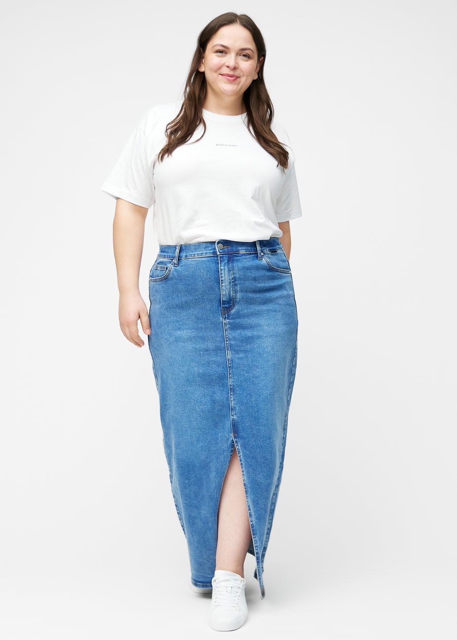 Plus-size model viser lang, klassisk blå denimnederdel i farven Rivers med regulær pasform i bevægelse og demonstrerer slids og materiale.